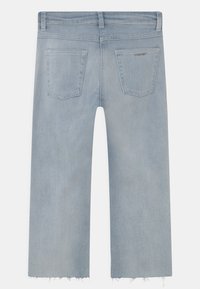 Jeans de denim azul claro com bainha crua e curta, apresentando dois bolsos traseiros e um detalhe de logotipo subtil perto do bolso direito.