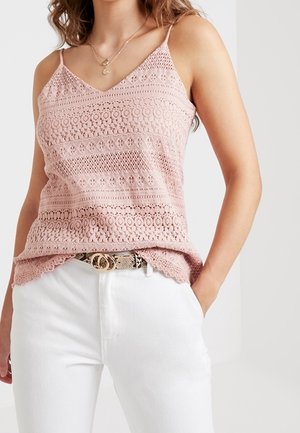 Blekt rosa spetslinne med djup V-ringning och tunna band, med horisontella mönster och vågiga kanter, kombinerat med vita byxor och ett skärp.