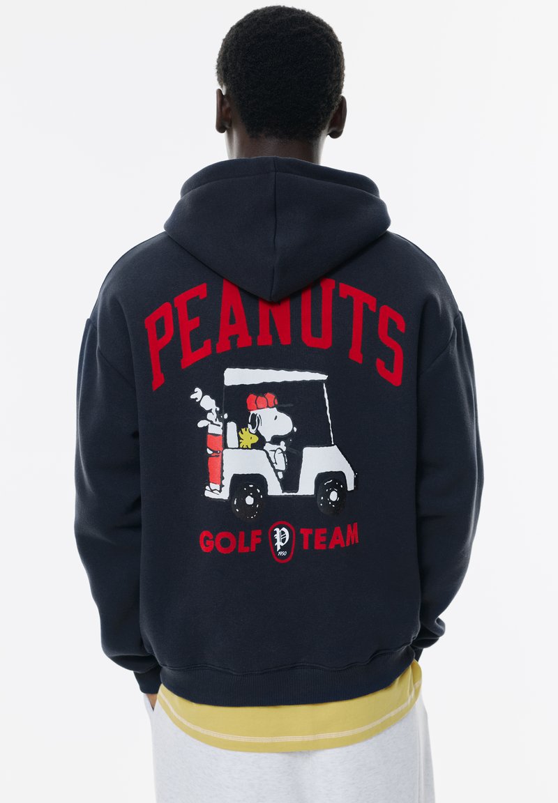 Hanorac bleumarin cu inscripția "ECHIPA DE GOLF PEANUTS" în roșu, completat cu o grafică a lui Snoopy și Woodstock într-un cart de golf. Fabricat dintr-un amestec de bumbac, are o croială lejeră și manșete ribbate.