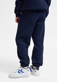 Granatowe spodnie dresowe wykonane z materiału bawełnianego, z elastycznymi ściągaczami i luźnym krojem, zestawione z białymi sneakersami z niebieskimi akcentami.