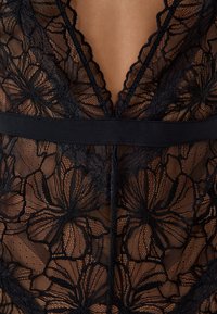 Indumento in pizzo nero con motivi floreali, scollatura profonda e una fascia nera solida in vita per una maggiore struttura.