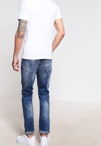 Camiseta blanca ajustada y jeans azules con un lavado desvanecido. Los jeans tienen un dobladillo enrollado y bolsillos traseros. El calzado son zapatillas blancas.