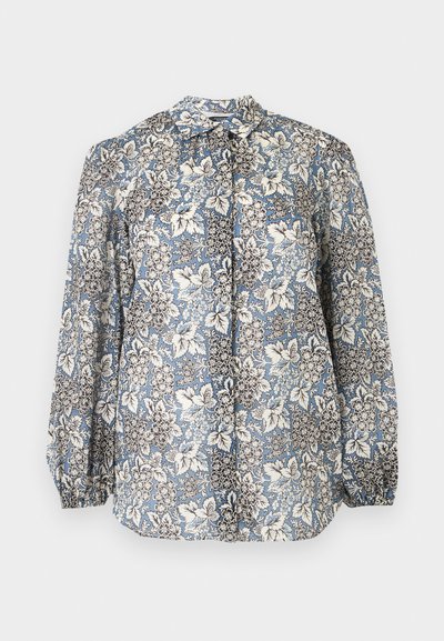 Blouse à manches longues avec motif floral bleu, blanc et noir, devant boutonné, poignets froncés sur fond gris clair.