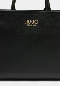 Sort læder totebag med struktureret overflade, prydet med guld LUJO MILANO-logo på fronten. Indeholder to robuste håndtag.