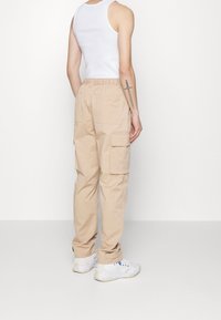Beige cargobyxor med resårmidja och flera fickor, i kombination med en vit linne och vita sneakers. Platt, slät textur.