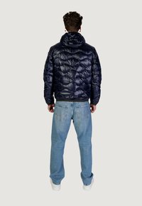 Giubbotto imbottito blu navy con motivo trapuntato e cappuccio, abbinato a jeans azzurri chiari e scarpe da ginnastica bianche. Presenta una vestibilità aderente in vita.