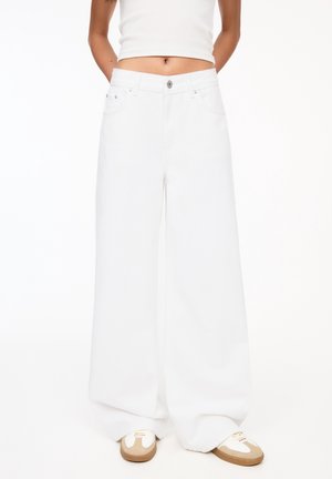 Woman wearing high-waist, wide-leg white pants paired with beige and white sneakers and a white cropped top.