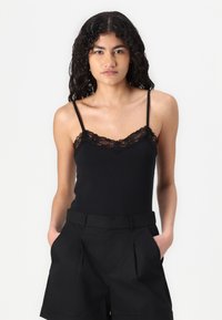 Svart topp med blonderkant, smale justerbare stropper og tettsittende design. Kombinert med høyMidje svarte shorts med sidelommer.