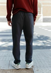Dunkelgraue Sporthosen mit elastischem Bund und seitlichen Taschen, kombiniert mit hellgrauen Sneakers mit grünen Akzenten.