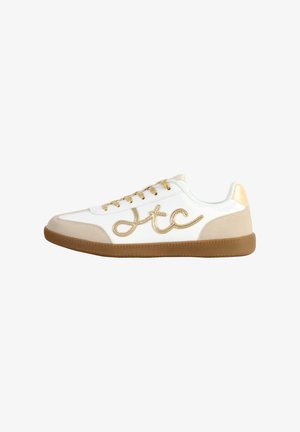 Zapatilla blanca con acentos dorados, con un upper de cuero suave, panel lateral texturizado, cordones planos y una suela de goma.