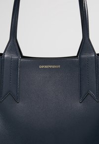 Navyblaue Leder-Shopper-Tasche mit strukturiertem Finish, ausgestattet mit stabilen Griffen und einem goldgeprägten "EMPORIO ARMANI"-Logo auf der Vorderseite.