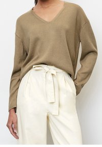 Maglione verde oliva a maglia testurizzata con scollatura a V abbinato a pantaloni crema a vita alta con dettaglio della vita legato.