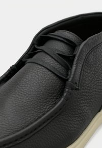 Μαύρο δερμάτινο παπούτσι με υφή στην επιφάνεια, διαθέτει στρογγυλεμένη μύτη, σύστημα κορδονιών και αντίθετη ανοιχτόχρωμη σόλα.