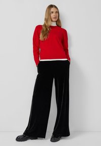 Rode trui met een witte halslijn, gecombineerd met zwarte wijde fluwelen broek en zwarte chunky schoenen. De stof lijkt zacht en gestructureerd.