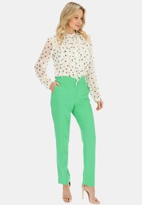 Biała bluzka w czarne kropki z falbankami, zestawiona z zielonymi spodniami wysokiego stanu i cielistymi sandałami na wysokim obcasie.
