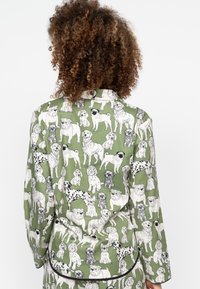 Zielona piżama z długim rękawem, pokryta ilustracjami czarno-białych psów, z kołnierzykiem w kształcie notcha i kontrastującym czarnym wykończeniem.