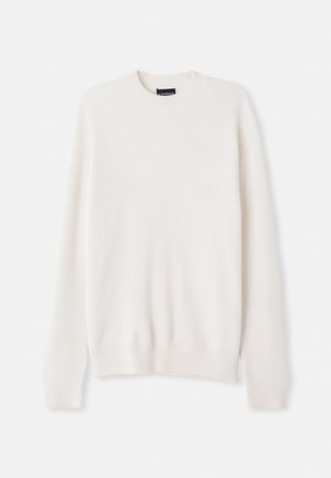 Pull en tricot côtelé blanc avec un col rond et des manches longues. Présente une petite broderie de logo sur la poitrine. Texture douce, design ajusté.