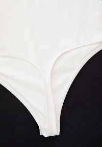 Parte bassa da nuoto bianca realizzata in tessuto liscio e elastico, con un design a taglio alto e cuciture minime, su uno sfondo nero.