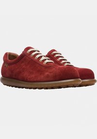 Sneaker rosse in suede con lacci crema e colletto imbottito. Presentano una superficie texturizzata e una suola in gomma marrone flessibile con punte arrotondate.