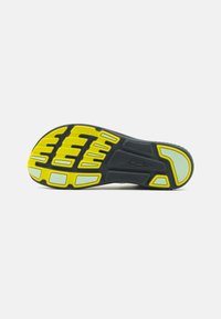 Semelle de chaussure en caoutchouc noir avec des motifs de traction jaunes et gris. Présente des rainures pour la flexibilité et l'adhérence, avec une surface texturée pour la durabilité.