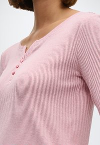 Ροζ ανοιχτό μπλούζα με μακριά μανίκια και οριζόντιες ρίγες, διαθέτει V-λαιμόκοψη και τρία κουμπιά στο λαιμό, υφασμάτινη υφή.