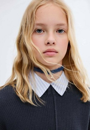 Dzianinowy ciemny sweter z wysokim kołnierzem, noszony na niebieskiej i białej koszuli w paski. Posiada długie, falujące blond włosy oraz niebieski choker.