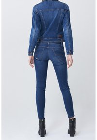 Denim jacket in dark blue, fitted design with two buttons at the waist. Slim fit blue jeans with back pockets, paired with black heeled ankle boots.