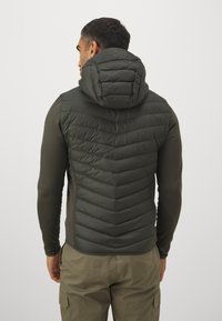 Groene gewatteerde vest met een chevronpatroon en een vaste capuchon. Heeft lange mouwen en een getailleerde stijl. Glad oppervlak, praktisch voor het dragen in lagen.