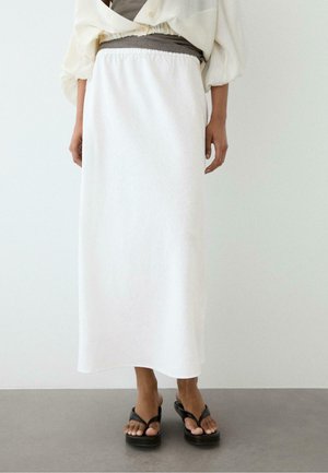 Frau trägt einen weißen Midirock mit hoher Taille und elastischem Bund, kombiniert mit schwarzen Plateausandalen und einem cremefarbenen Oberteil mit Puffärmeln.