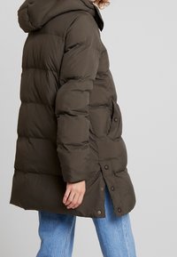 Puffjakke i mørke olivengrøn med hætte, quiltet design, sidelommer og trykknaplukninger. Glat tekstur og længde til midt på låret.