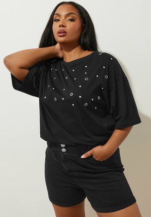 Maglietta nera oversize con dettagli metallici e vestibilità ampia, abbinata a pantaloni corti in denim neri con vita rilassata e dettagli con bottoni.