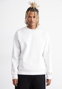 Lys grå sweatshirt med raglanærmer, ribstrikkede manchetter og kant. Har et lille gult logo ved manchetten. Blødt bomuldsblandingsmateriale.