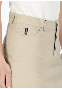Beige cotton skirt with a high waist, front buttons, and a subtle anchor embroidery on the side. Features a logo tag on the pocket.