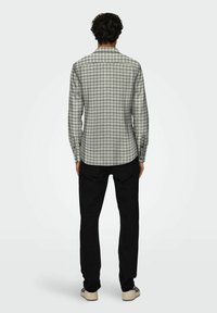 Camisa de cuadros en gris y negro, de manga larga con cuello puntiagudo. Combinada con pantalones negros y zapatillas de color claro. Diseño trasero sencillo.