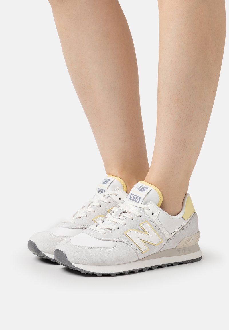 Vita och gula New Balance 574 sneakers i mocka och textil, med en vadderad sula och snörningsdesign.