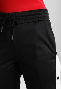 Svarta joggerbyxor med texturerad yta, med dragsko i midjan, vita sidostripes och tryckknappdetaljer.