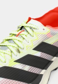 Αθλητικό παπούτσι σε πράσινο λάιμ και λευκό, με ανώτερο μέρος από δίχτυ, μαύρες ρίγες και υφασμένο λαστιχένιο πέλμα. Διαθέτει φλούο κορδόνια και κόκκινη λεπτομέρεια στη γλώσσα.