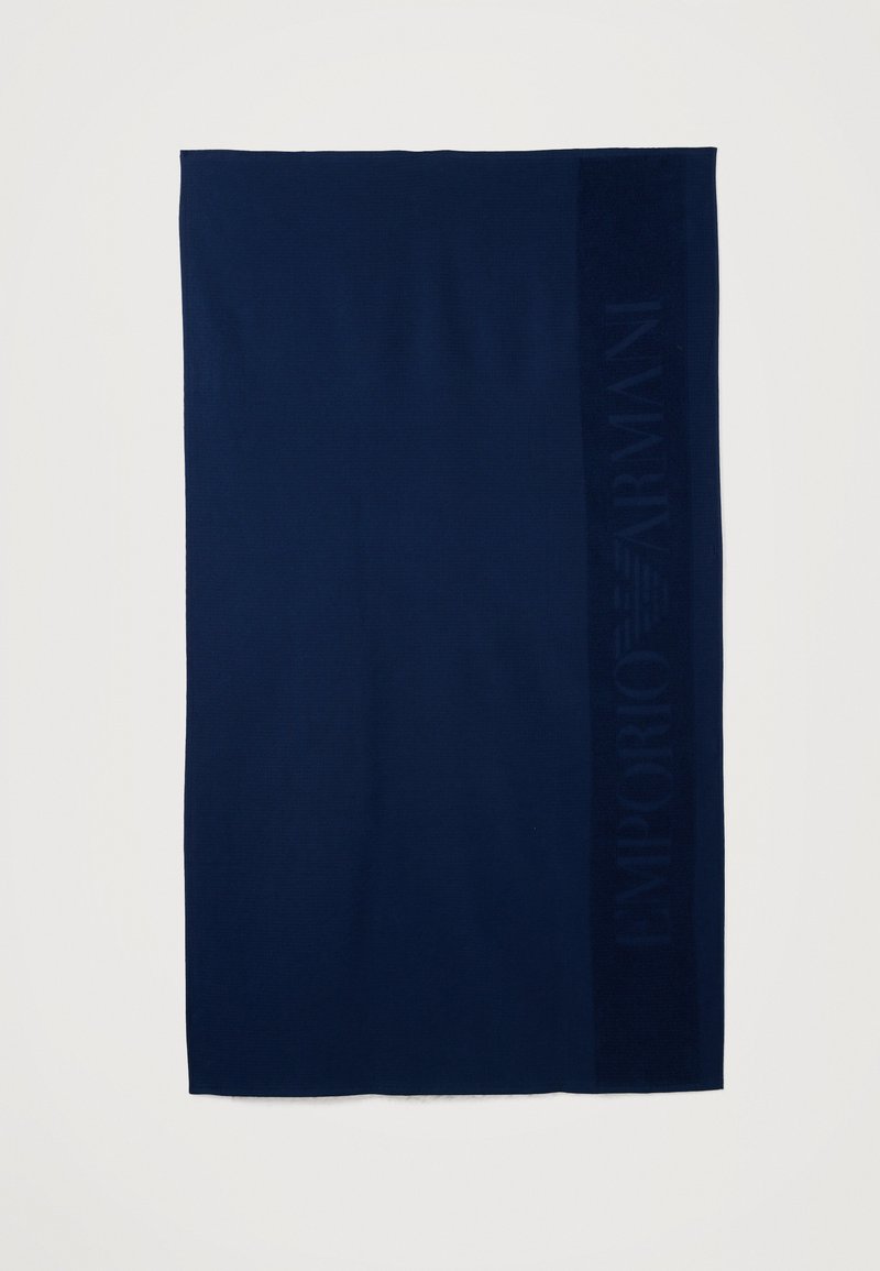 Σκούρο μπλε ορθογώνιο ύφασμα με διακριτική ανάγλυφη κάθετη λωρίδα που εμφανίζει το κείμενο "EMPORIO ARMANI" στη δεξιά πλευρά.