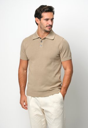 Polo shirt beige a maniche corte con un motivo a maglia testurizzato, colletto a due bottoni e orlo solido, abbinato a pantaloni chiari.