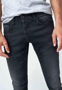 Jeans de mezclilla negra con cinco bolsillos, cierre de botón y diseño ajustado. La tela tiene una textura suave con un ligero desgaste.