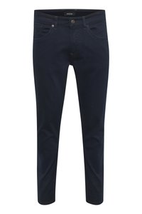 Granatowe dżinsy o slim fit, pięć kieszeni, widoczny szew oraz metalowy guzik na pasku.
