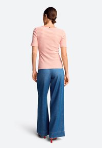 Striped short-sleeve top in coral and white, paired with wide-leg blue denim pants, featuring a hem detail and red heels.