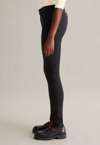 Czarne wąskie dżinsy z wysokim stanem, o gładkiej fakturze denimu i minimalnych dodatkach, w połączeniu z masywnymi czarnymi loafersami.