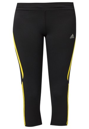 Leggings de sport noirs avec des bandes latérales jaunes et un petit logo blanc Adidas sur la cuisse supérieure.