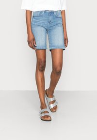 Pantalones cortos de mezclilla azul claro con un corte recto y un ligero deshilachado en el dobladillo, combinados con sandalias metálicas plateadas con hebillas ajustables.