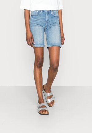 Pantalones cortos de mezclilla azul claro con un corte recto y un ligero deshilachado en el dobladillo, combinados con sandalias metálicas plateadas con hebillas ajustables.