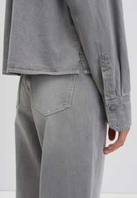 Gray denim shirt with long sleeves, side slits, and buttoned cuffs. Paired with matching gray high-waisted pants featuring back pockets.
