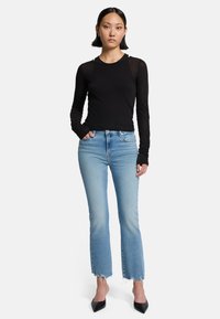 Schwarzes Langarmshirt mit figurbetontem Design, kombiniert mit hellblauen Jeans mit ausgefranstem Saum, abgerundet mit schwarzen spitzen High Heels.