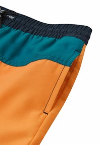 Shorts en tissu orange et teal, dotés d'une taille élastique avec une texture froncée et des détails de couture contrastants le long des coutures.