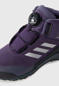 Lila Sportschuh mit strukturiertem Obermaterial, schwarzen Akzenten, flexibler Sohle und einem BOA-Schnürsystem für einen sicheren Sitz. Silbernes Logo und Streifen.